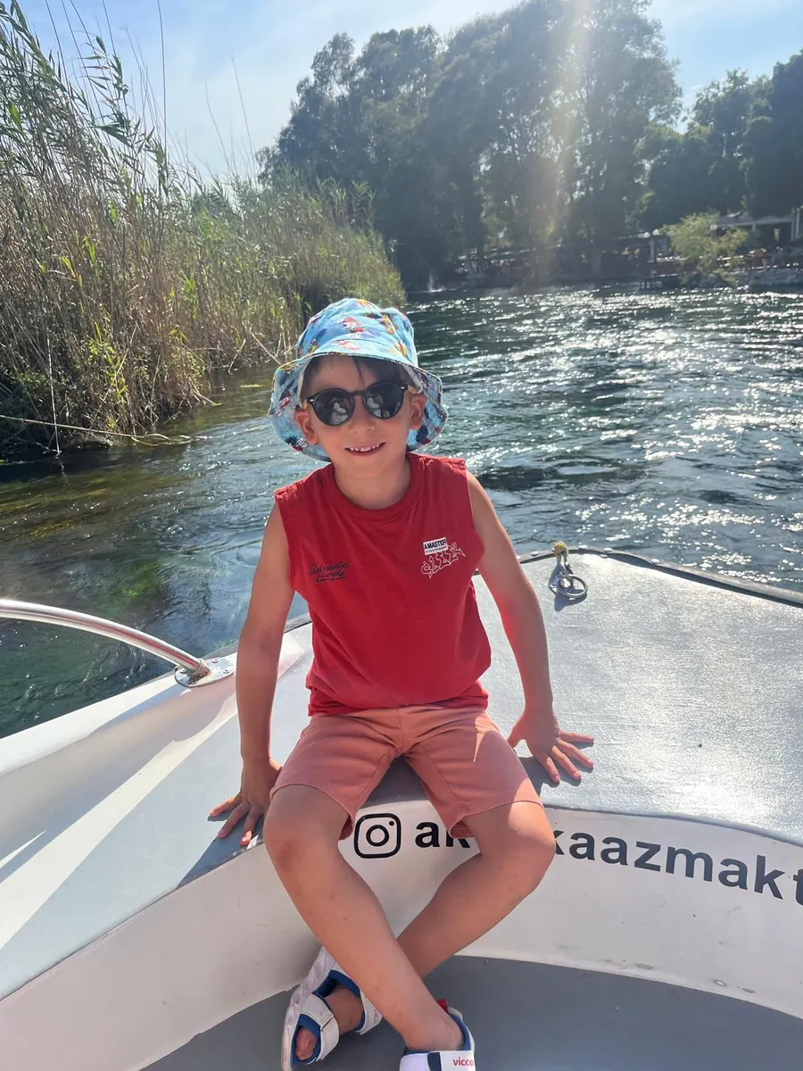 Aras, güneş gözlüğü ve şapkasıyla teknenin burnunda oturuyor