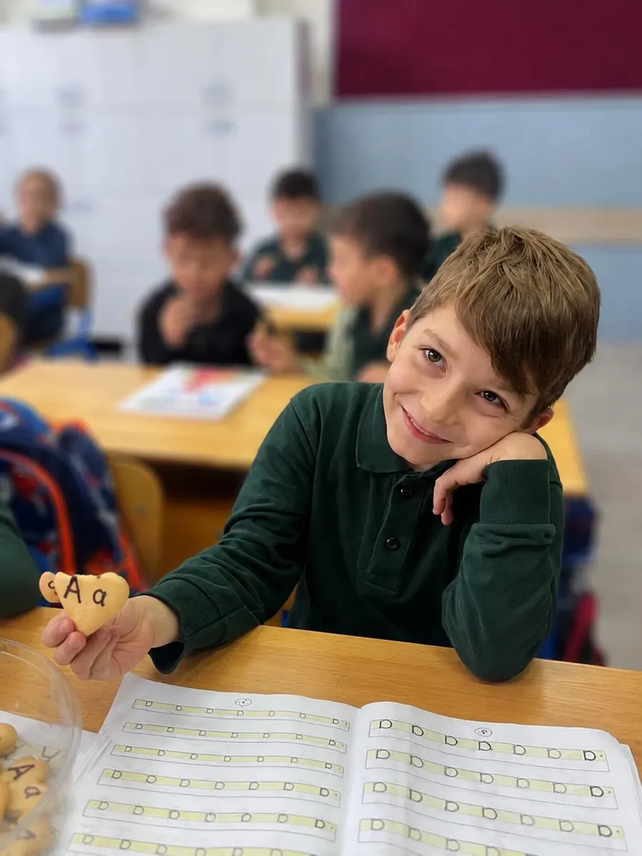 Aras, sınıfta elindeki kalp şeklindeki A harfli kurabiyeyle gülümsüyor